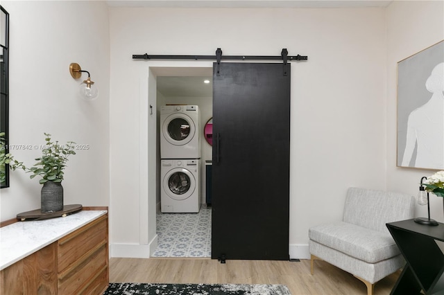 clothes washing area featuring stacked washer / dryer, a barn door, and light hardwood / wood-style flooring