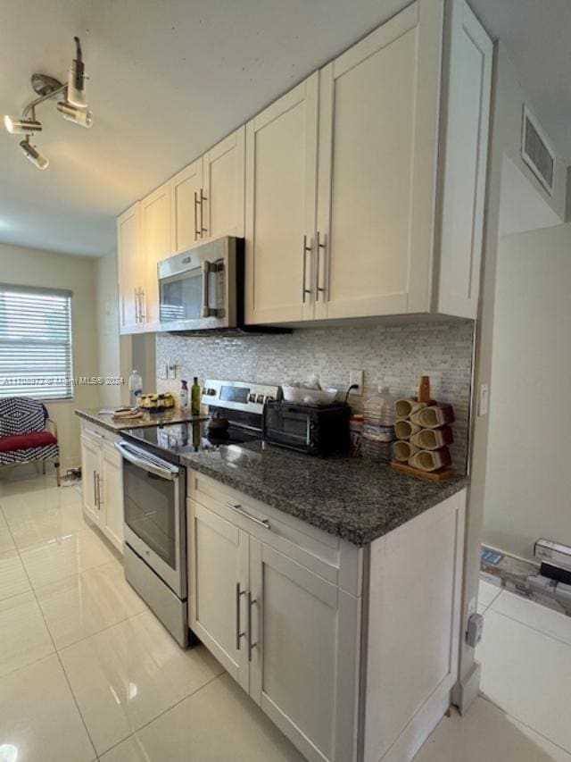 kitchen with appliances with stainless steel finishes, tasteful backsplash, white cabinetry, and dark stone counters