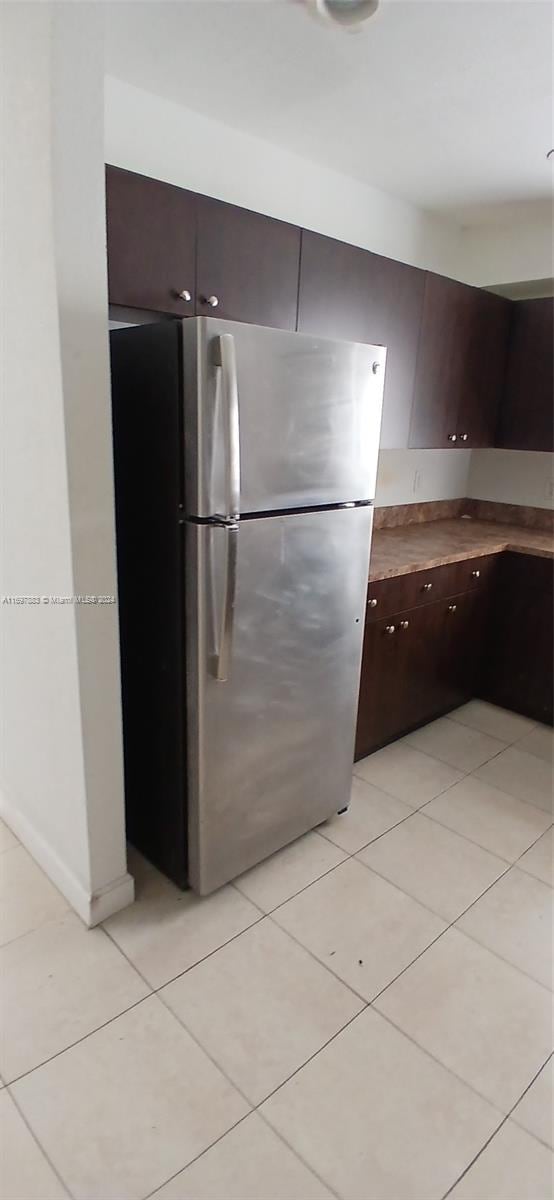 kitchen with stainless steel refrigerator, dark brown cabinetry, and light tile patterned floors