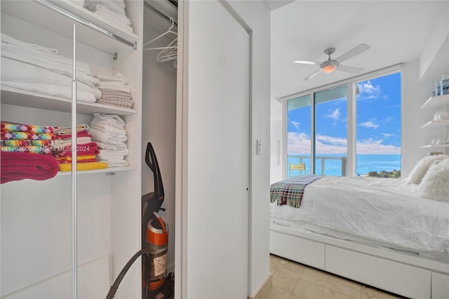 bedroom featuring ceiling fan, a closet, a water view, and light tile patterned flooring