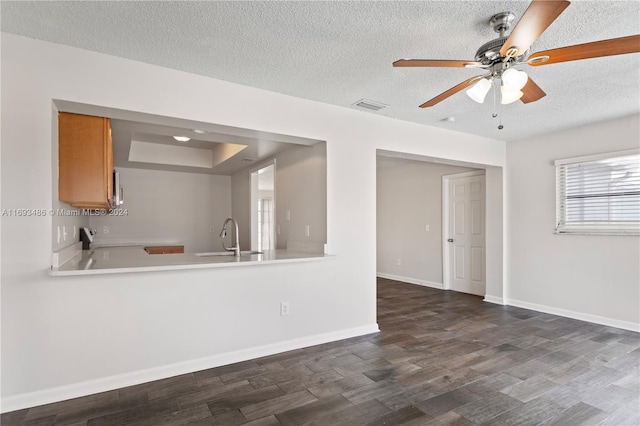 interior space featuring ceiling fan, sink, dark wood-type flooring, a textured ceiling, and a tray ceiling