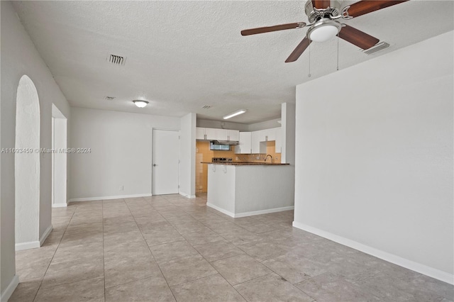 unfurnished living room featuring ceiling fan, sink, light tile patterned floors, and a textured ceiling