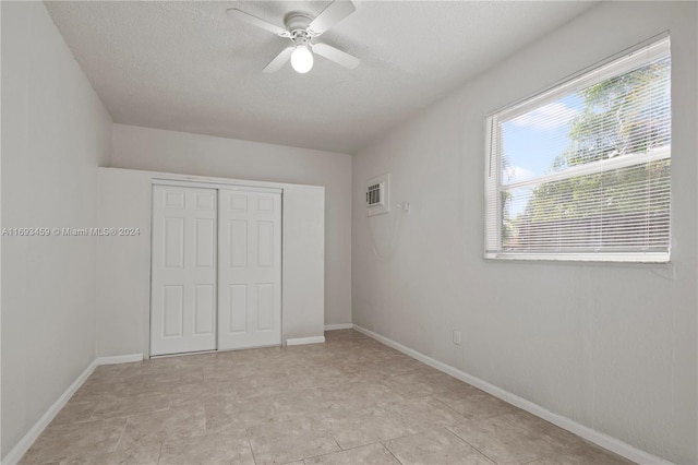 unfurnished bedroom featuring a textured ceiling, a closet, ceiling fan, and light tile patterned flooring