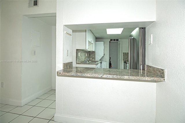 kitchen with white cabinets, kitchen peninsula, light tile patterned floors, and backsplash