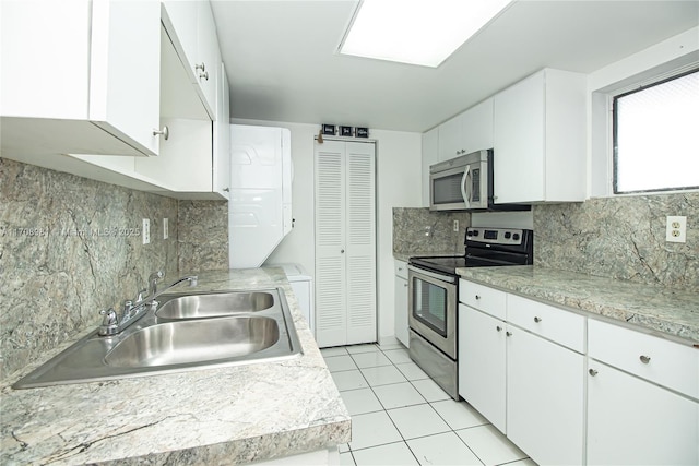 kitchen with backsplash, sink, light tile patterned floors, appliances with stainless steel finishes, and white cabinetry