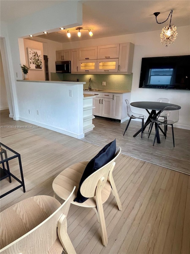 kitchen featuring tasteful backsplash, sink, light hardwood / wood-style flooring, a notable chandelier, and white cabinets