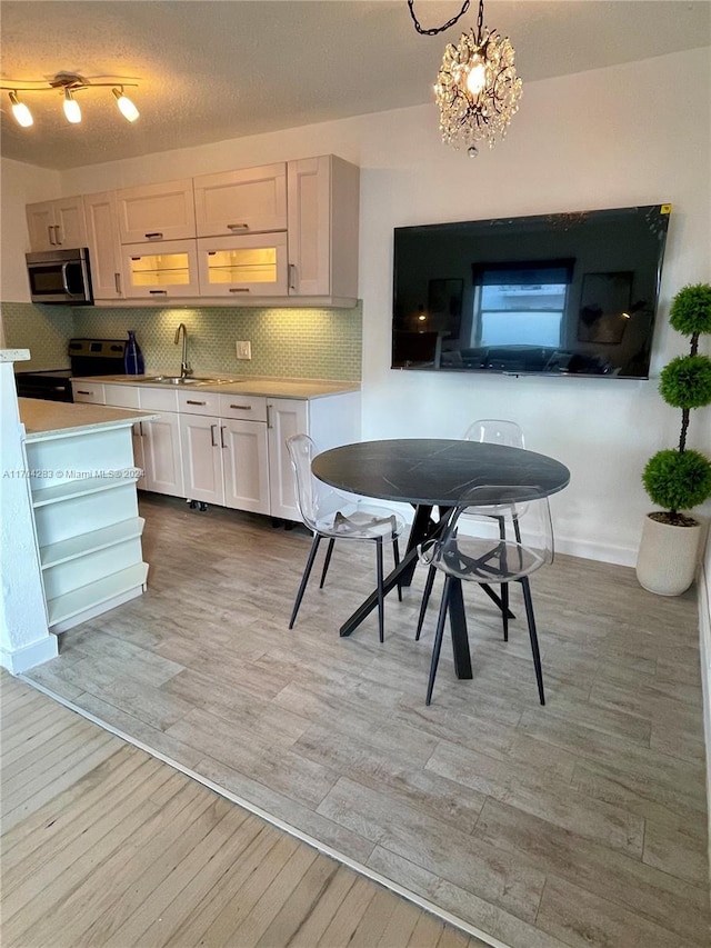 kitchen with white cabinetry, stainless steel appliances, hanging light fixtures, a notable chandelier, and light hardwood / wood-style floors