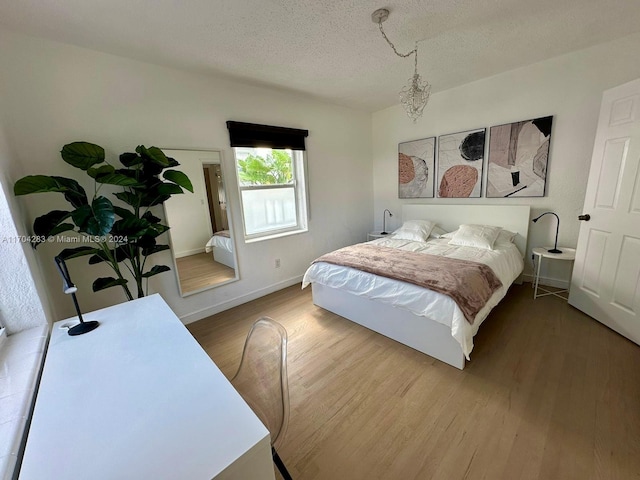 bedroom featuring an inviting chandelier, a textured ceiling, and hardwood / wood-style flooring