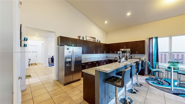 kitchen featuring stainless steel appliances, high vaulted ceiling, a kitchen bar, a kitchen island with sink, and dark brown cabinets