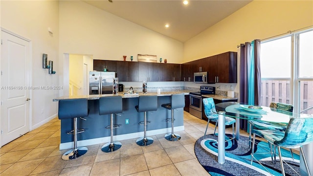 kitchen with a kitchen island with sink, high vaulted ceiling, a kitchen breakfast bar, dark brown cabinets, and stainless steel appliances