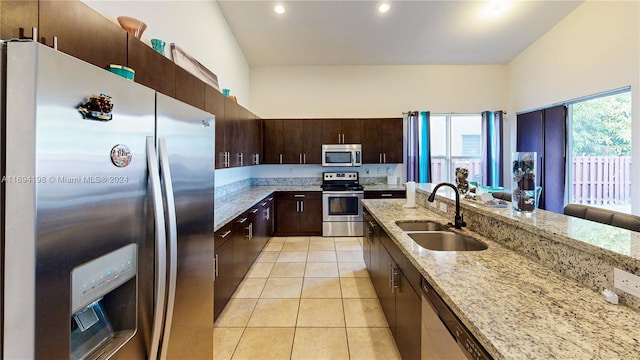 kitchen with light stone counters, dark brown cabinetry, stainless steel appliances, sink, and light tile patterned flooring