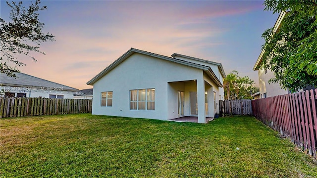 back house at dusk featuring a lawn