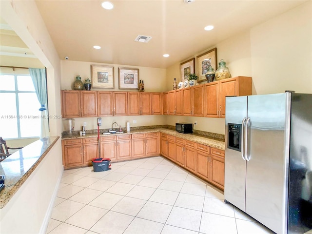 kitchen with stainless steel fridge, light stone counters, light tile patterned floors, and sink