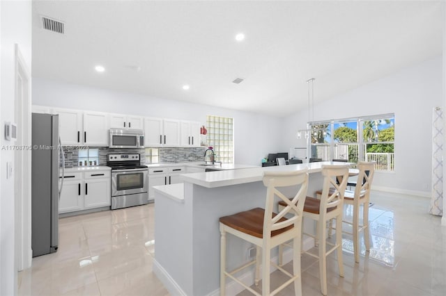 kitchen with white cabinets, vaulted ceiling, appliances with stainless steel finishes, tasteful backsplash, and a breakfast bar area