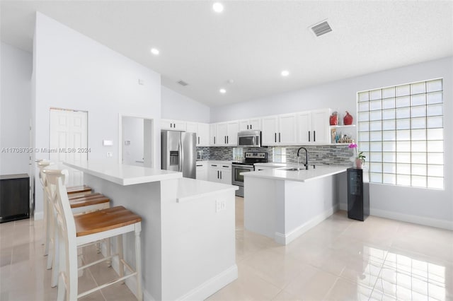 kitchen featuring kitchen peninsula, light tile patterned floors, appliances with stainless steel finishes, a kitchen bar, and white cabinetry