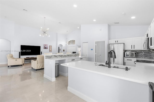 kitchen featuring appliances with stainless steel finishes, high vaulted ceiling, white cabinetry, hanging light fixtures, and an island with sink