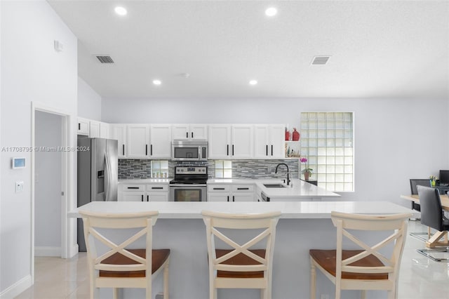 kitchen featuring sink, appliances with stainless steel finishes, white cabinetry, kitchen peninsula, and a breakfast bar area