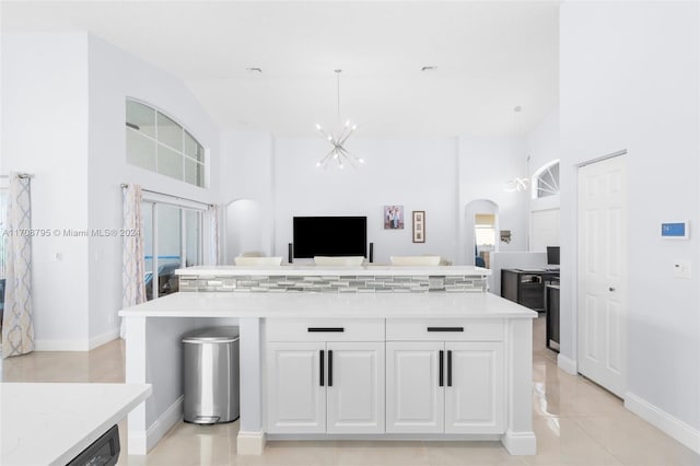 kitchen featuring a towering ceiling, light tile patterned floors, white cabinets, a center island, and hanging light fixtures