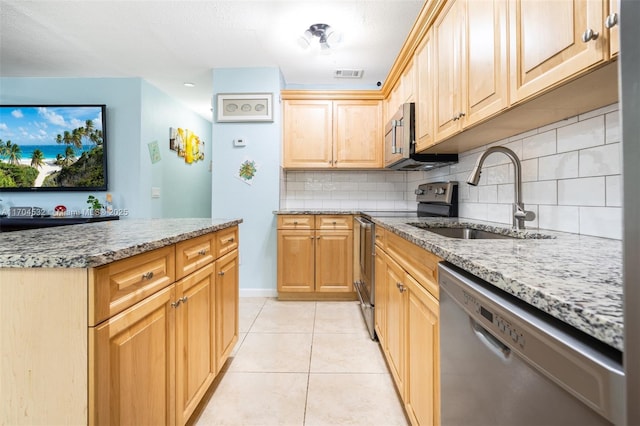 kitchen featuring backsplash, sink, light stone countertops, appliances with stainless steel finishes, and light tile patterned flooring