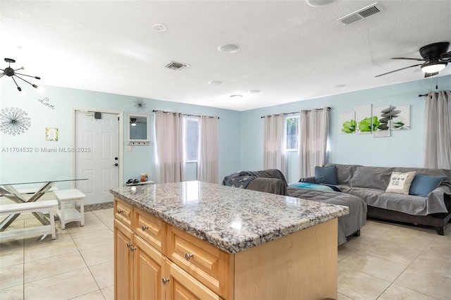 kitchen featuring a center island, ceiling fan, light tile patterned floors, a textured ceiling, and light stone counters