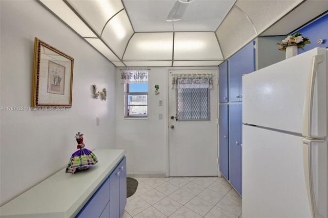 kitchen with light tile patterned floors, white fridge, and blue cabinets