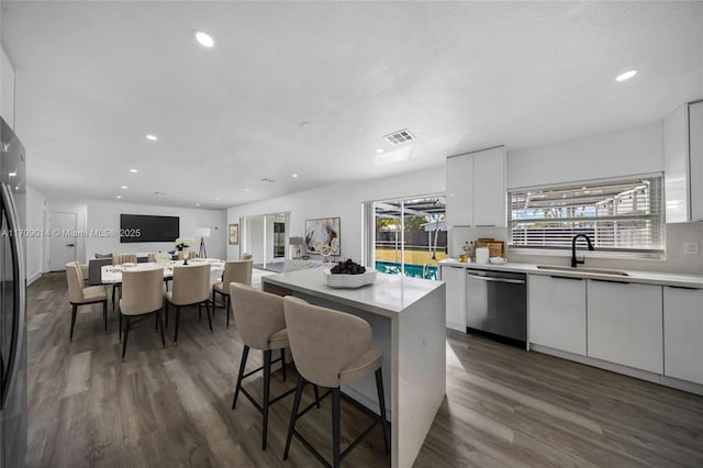 kitchen featuring sink, a kitchen island, stainless steel dishwasher, a breakfast bar area, and white cabinets