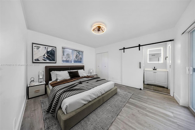 bedroom with a barn door, light hardwood / wood-style flooring, and ensuite bath