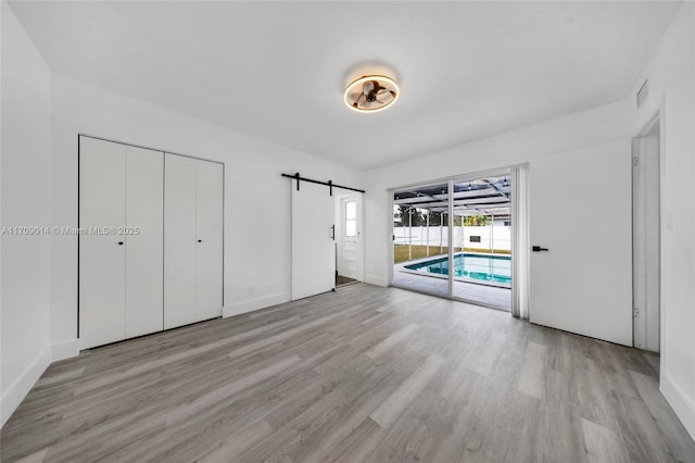 unfurnished bedroom featuring access to exterior, light wood-type flooring, a barn door, and a closet