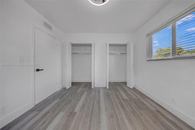 unfurnished bedroom with light wood-type flooring and multiple closets