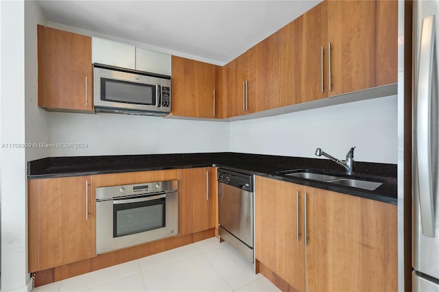 kitchen featuring light tile patterned floors, stainless steel appliances, dark stone counters, and sink