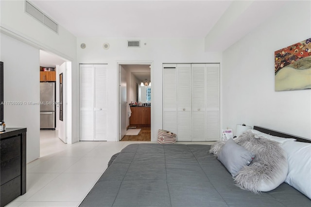 bedroom with stainless steel refrigerator, connected bathroom, and an inviting chandelier