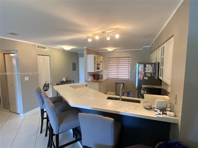 kitchen featuring kitchen peninsula, stainless steel fridge, light tile patterned floors, white cabinets, and a breakfast bar area