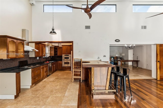 kitchen featuring a high ceiling, stainless steel appliances, tasteful backsplash, and pendant lighting