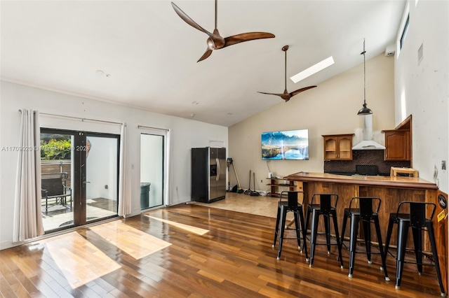 kitchen featuring backsplash, wall chimney range hood, stainless steel refrigerator with ice dispenser, hardwood / wood-style flooring, and a breakfast bar area