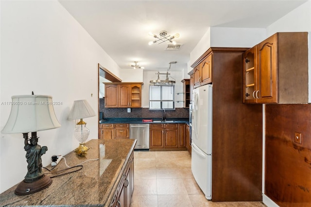 kitchen featuring backsplash, stainless steel dishwasher, sink, dark stone countertops, and white fridge