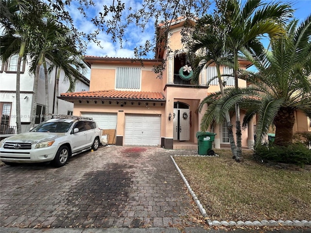 mediterranean / spanish house with a balcony, an attached garage, stucco siding, a tiled roof, and decorative driveway