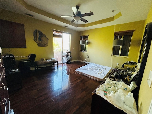 living area featuring visible vents, ceiling fan, a tray ceiling, and wood finished floors