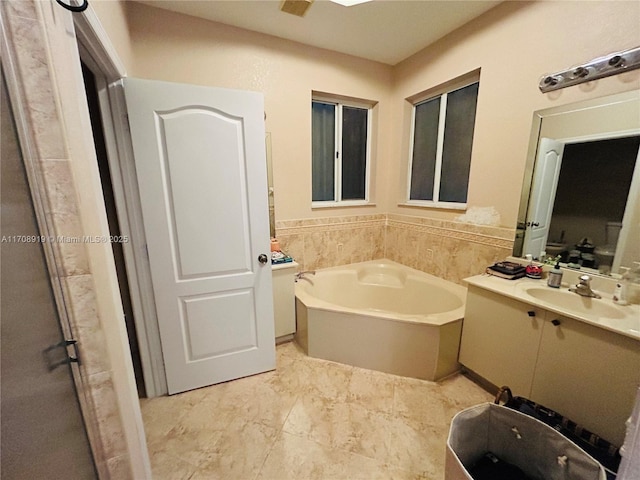 full bathroom featuring wainscoting, a bath, and vanity