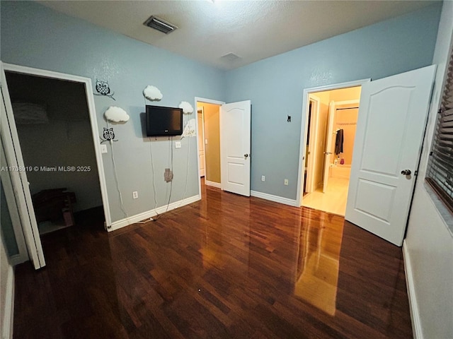 unfurnished bedroom featuring visible vents, connected bathroom, baseboards, and wood finished floors