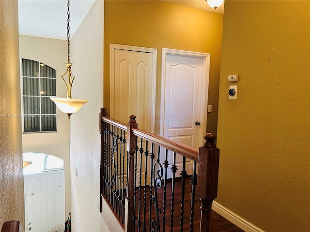 corridor with an upstairs landing, a textured wall, baseboards, and wood finished floors