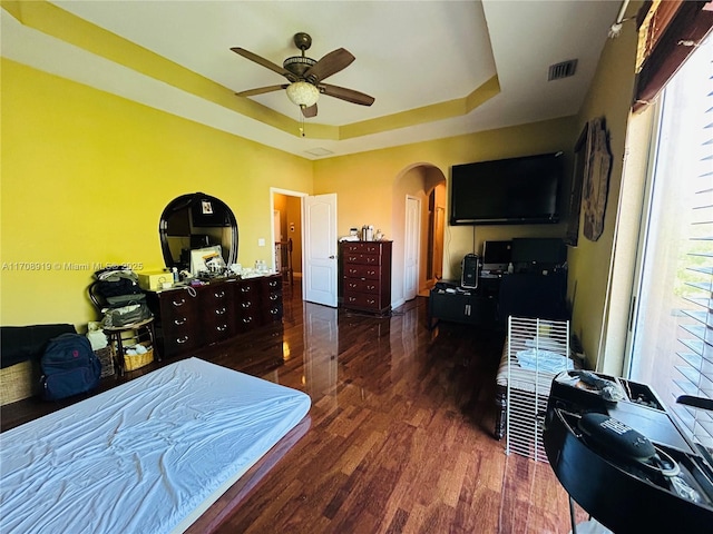 bedroom featuring arched walkways, multiple windows, a tray ceiling, and wood finished floors