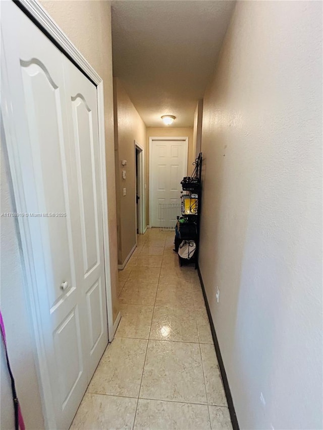 corridor featuring baseboards and light tile patterned flooring