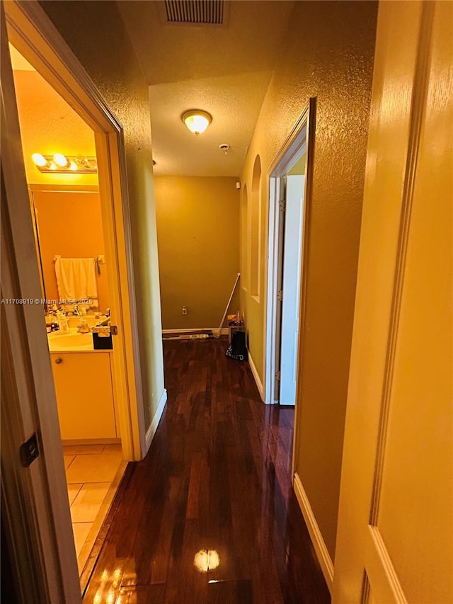 hallway featuring a textured wall, visible vents, baseboards, and wood finished floors