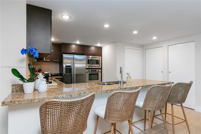 kitchen with kitchen peninsula, dark brown cabinetry, stainless steel appliances, and sink