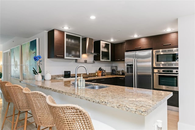 kitchen featuring sink, wall chimney exhaust hood, dark brown cabinets, kitchen peninsula, and stainless steel appliances