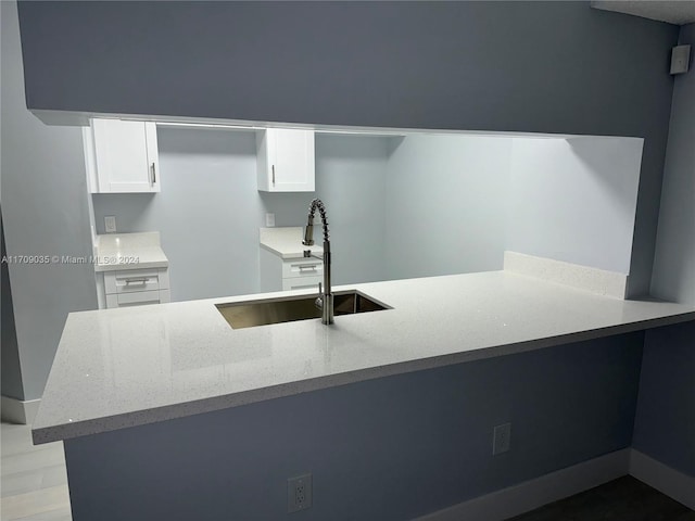 kitchen featuring sink, light stone countertops, light wood-type flooring, white cabinetry, and kitchen peninsula