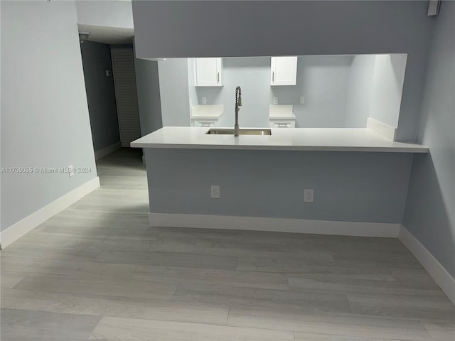 kitchen with kitchen peninsula, sink, white cabinets, and light hardwood / wood-style flooring