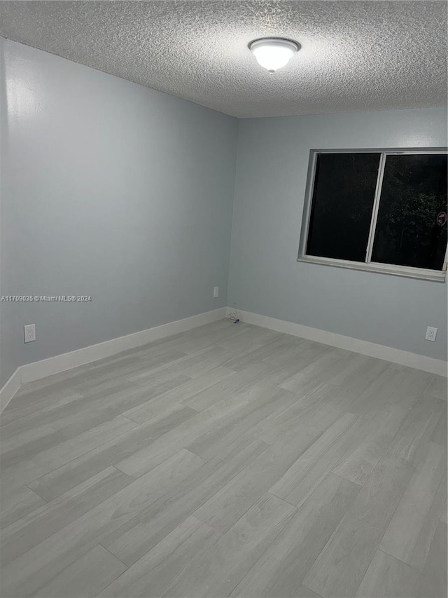 unfurnished room with light hardwood / wood-style flooring and a textured ceiling