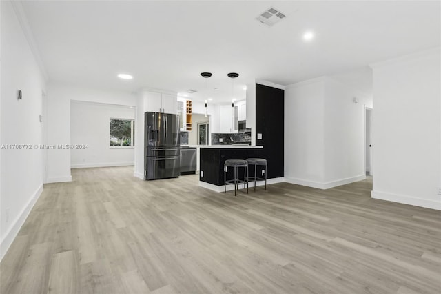 kitchen featuring crown molding, light wood-type flooring, appliances with stainless steel finishes, a kitchen bar, and white cabinetry