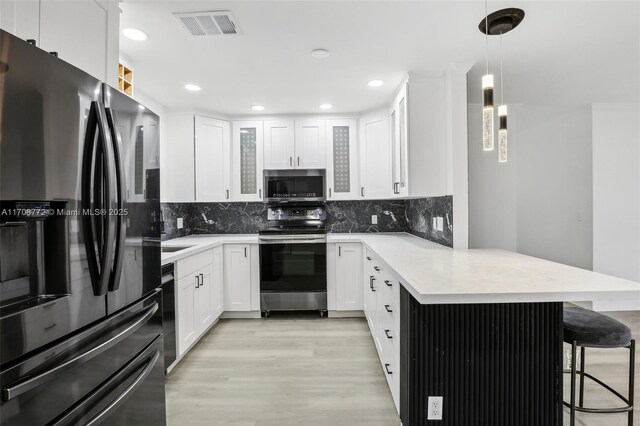 524 NW 7th Ct, Boynton Beach, FL 33426 - kitchen with stainless steel appliances, a peninsula, a breakfast bar area, light wood-style flooring, and white cabinetry